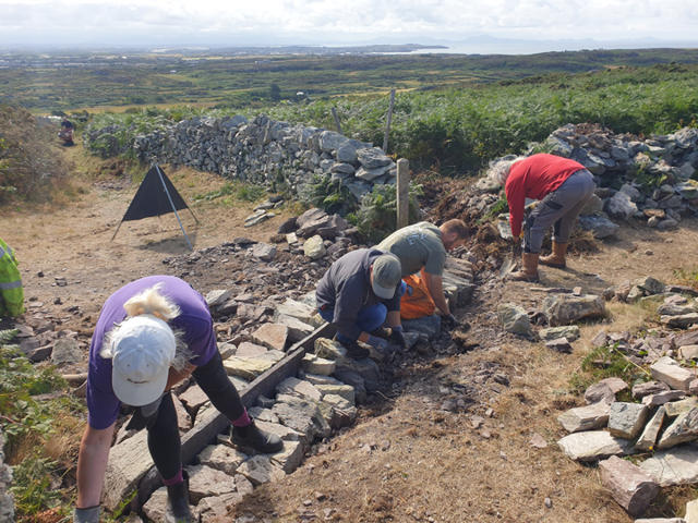 Gwirfoddolwyr yn gosod cerrig i greu toriad dŵr